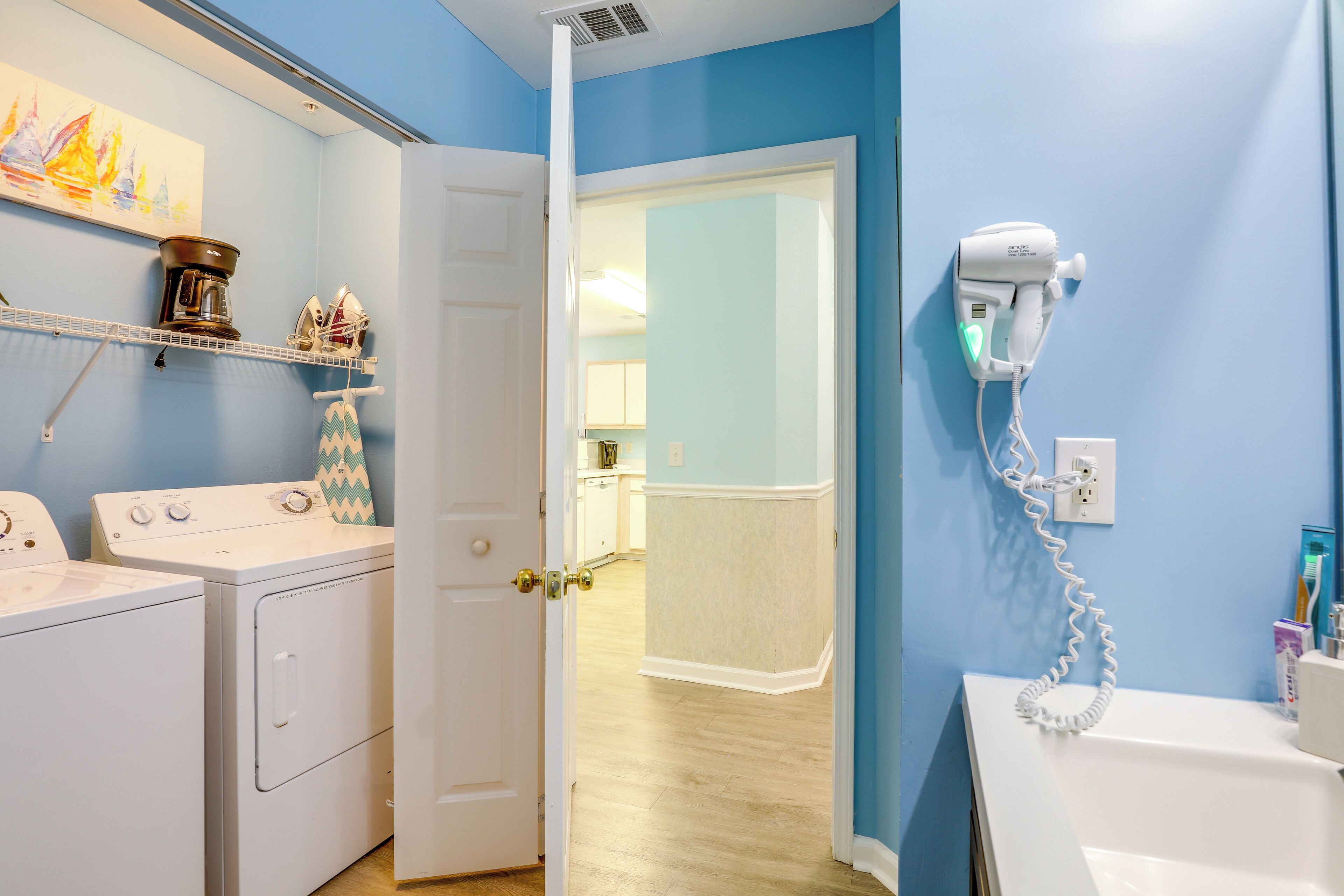 A laundry room with a washer and dryer, a hairdryer on a wall, and a door leading to a hallway.