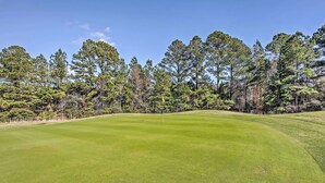 A golf course with a well-maintained green, surrounded by tall pine trees. - Swim, Golf & Relax: Resort Condo in Myrtle Beach! (Myrtle Beach)