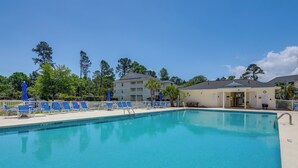 A swimming pool with blue chairs and a building in the background. - Swim, Golf & Relax: Resort Condo in Myrtle Beach! (Myrtle Beach)