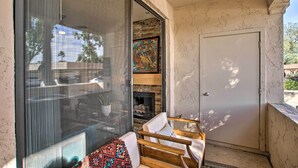 A balcony with a glass door, a white chair, a patterned throw pillow, and a fireplace. - Balconies & Resort Amenities: Scottsdale Condo (Scottsdale)