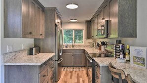 A modern kitchen with wooden cabinets, granite countertops, a built-in oven, and a stainless steel refrigerator. - Waterfront Troutdale Hideaway: Sandy River Fishing (Troutdale)