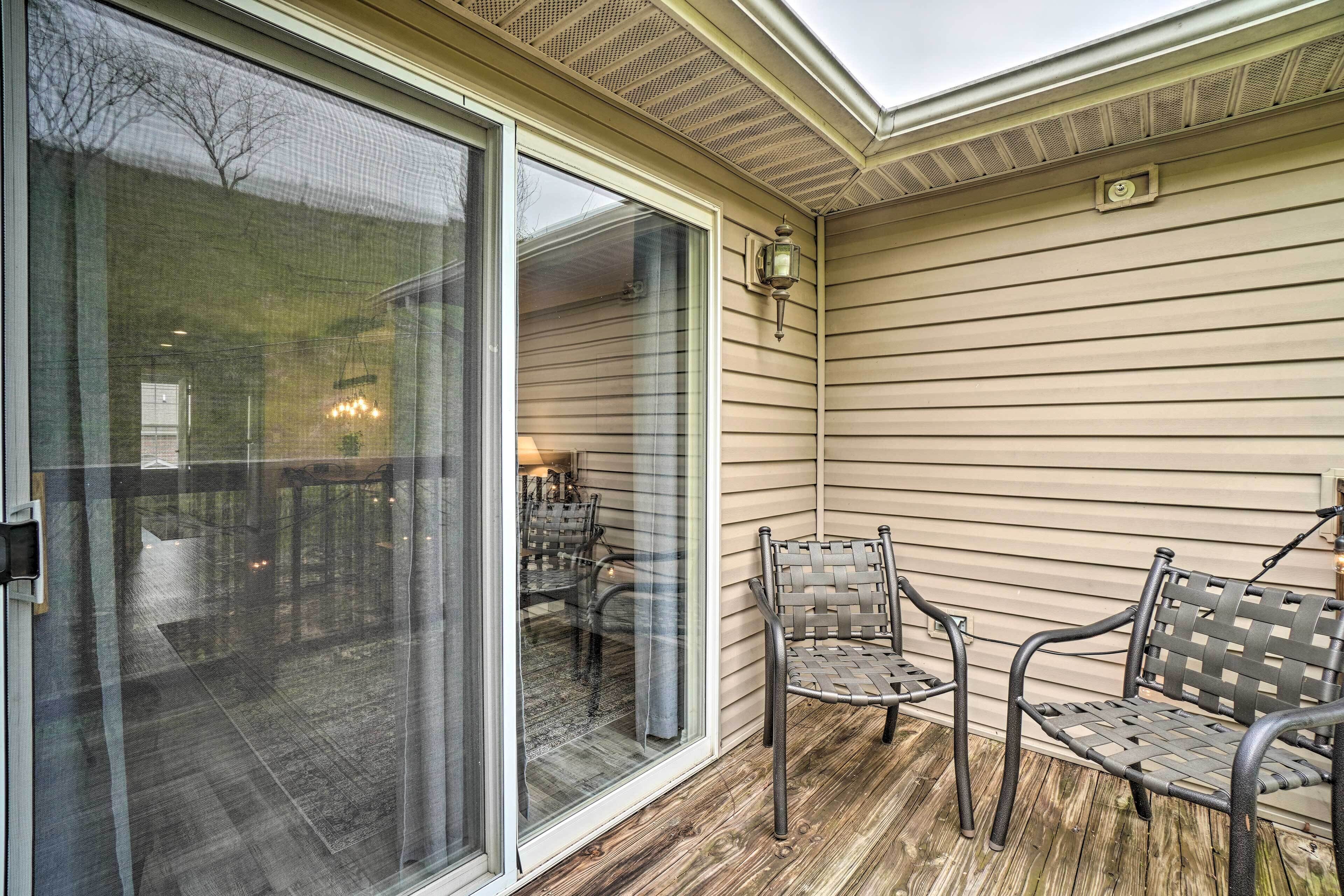A covered patio with two metal chairs and a table, a sliding glass door leading to an interior space, and a ceiling vent.
