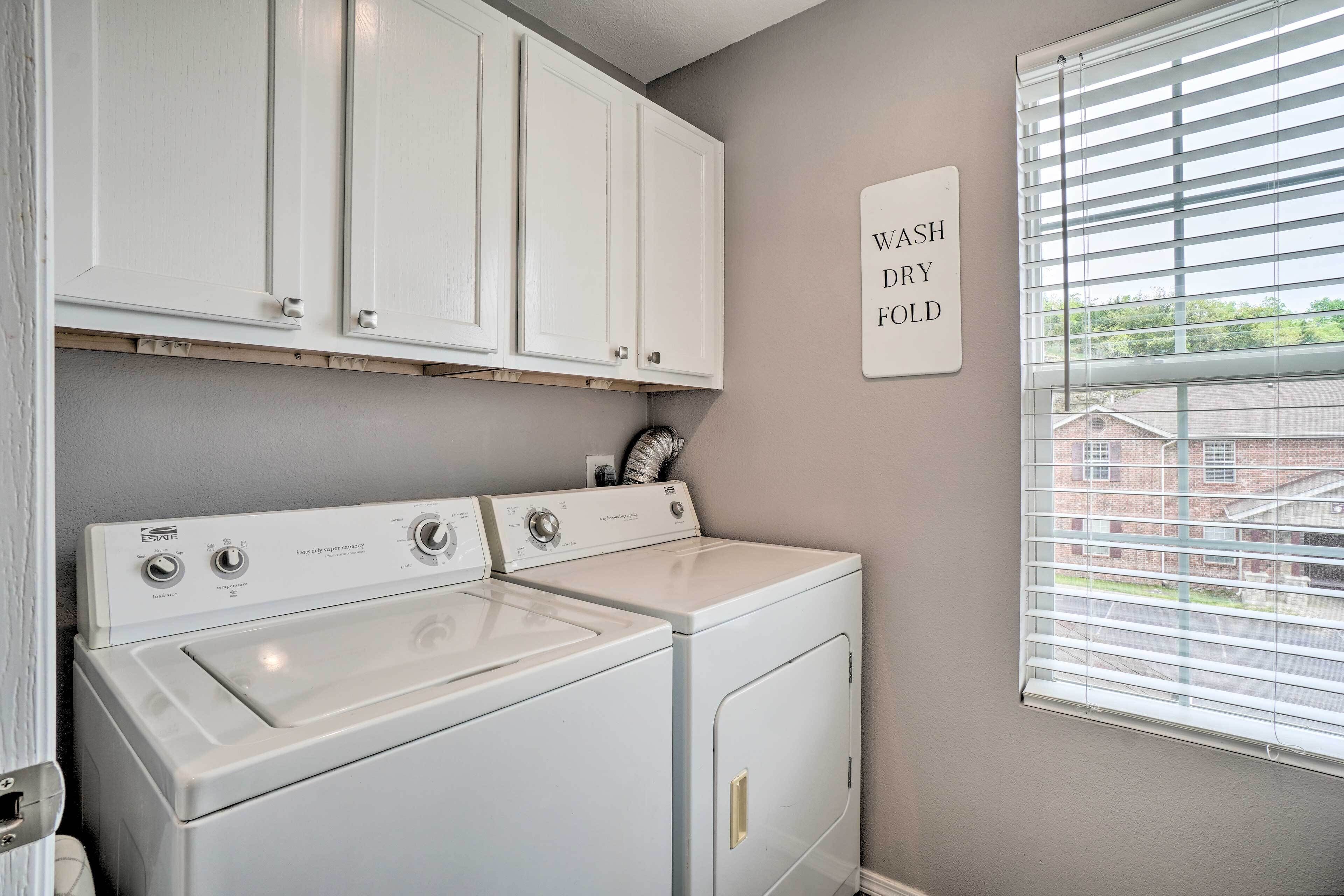 A laundry room with a washer and dryer, white cabinets above, and a window with blinds.