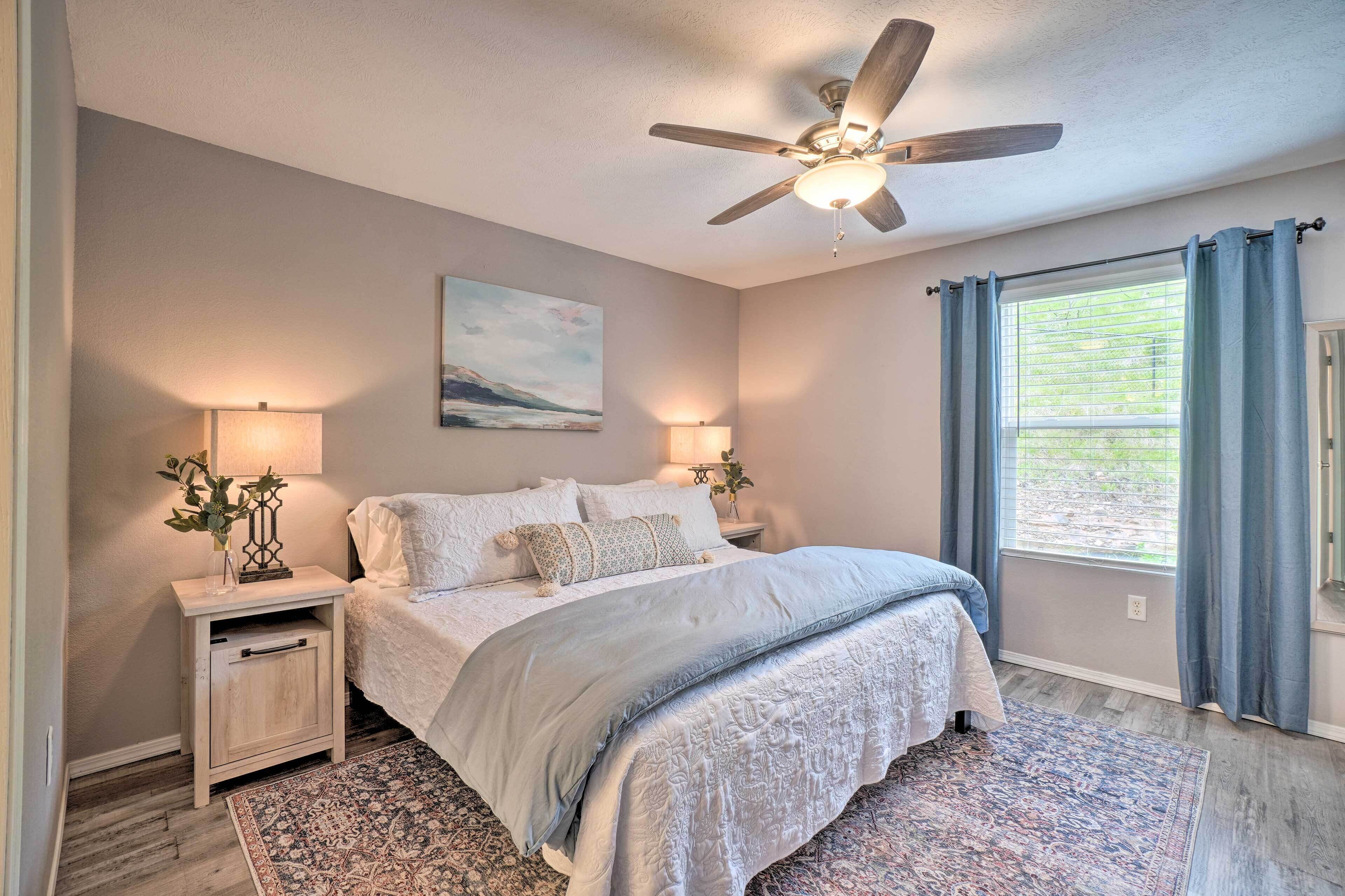A bedroom with a bed, bedside lamps, a ceiling fan, a window with curtains, and a rug.