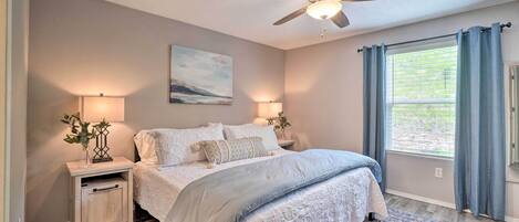A bedroom with a bed, bedside lamps, a ceiling fan, a window with curtains, and a rug.