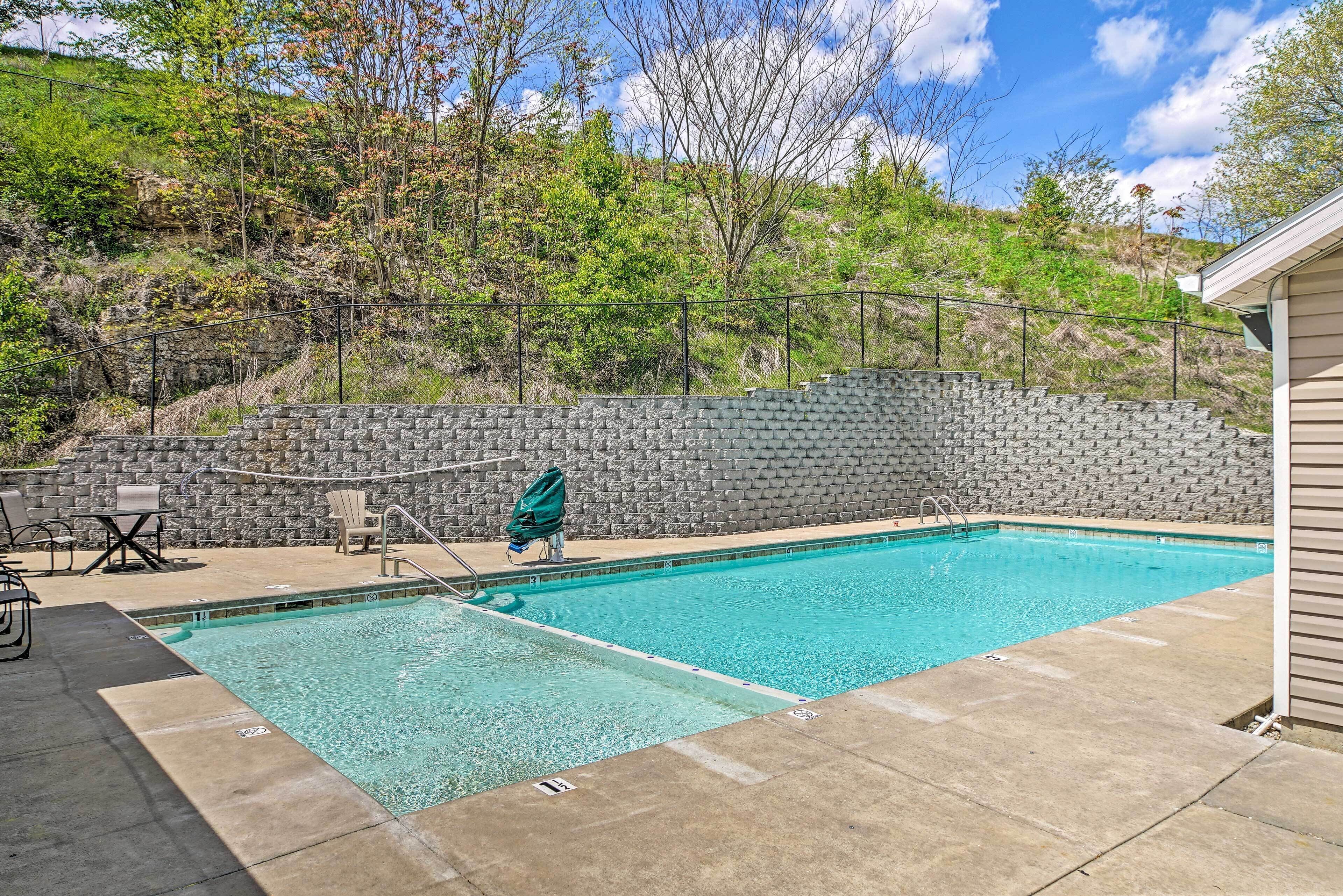 Une piscine rectangulaire avec un mur en pierre en arrière-plan, un espace de détente avec des chaises et une table, et un ciel dégagé au-dessus.