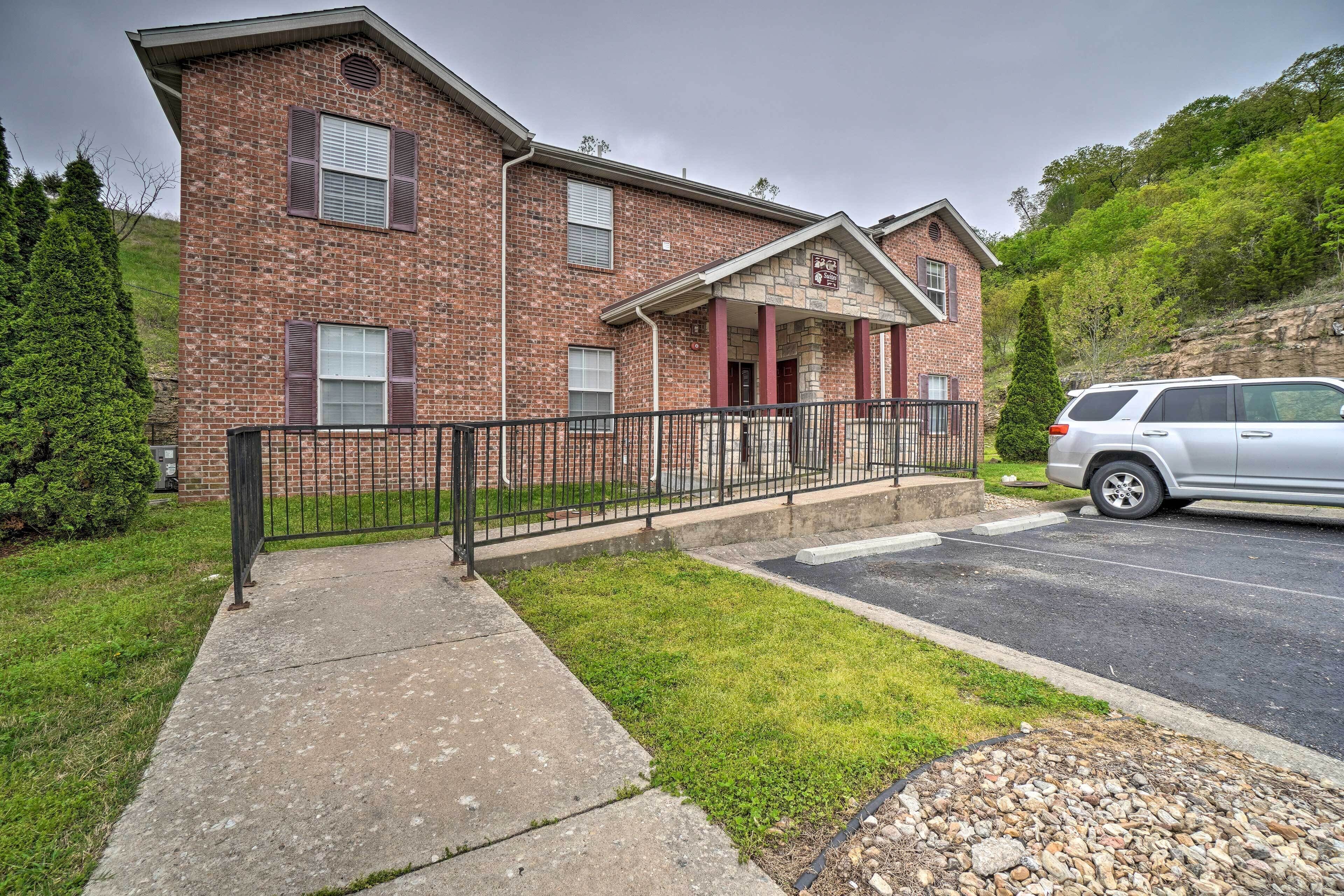 A two-story brick building with a covered porch, a parking area, and a grassy lawn.