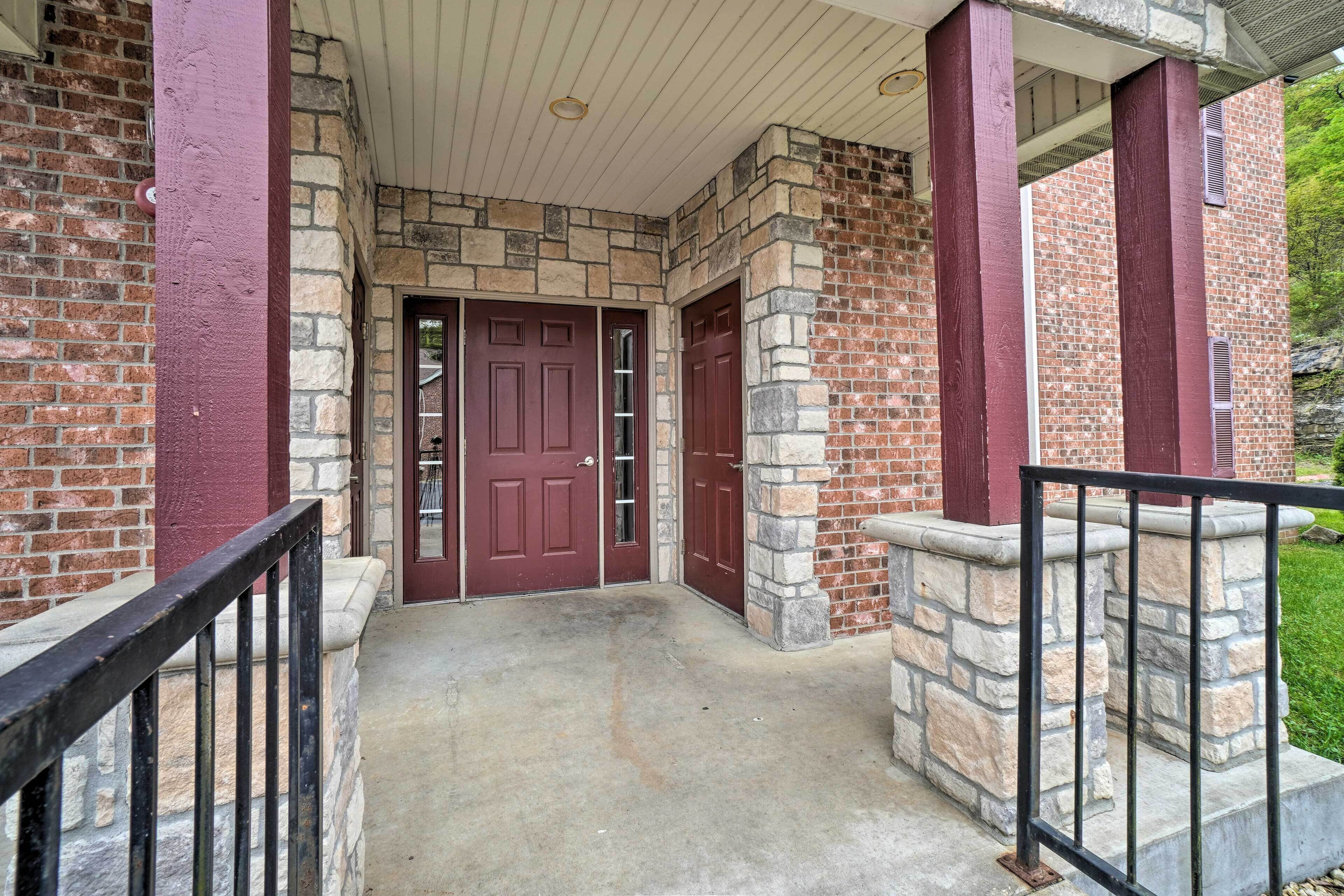 A building entrance with a red door, stone and brick walls, and a concrete porch.