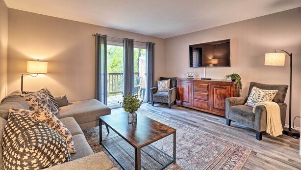 A living room with a sofa, armchair, coffee table, and a flat-screen TV mounted on the wall. - Modern Condo w/ Deck ~ 7 Mi To Branson Landing! (Branson)