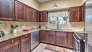 A kitchen with dark wooden cabinets, a granite countertop, stainless steel appliances, and a window with a curtain. - Relaxing Green Valley Townhome ~ 30 Mi to Tucson! (Green Valley)