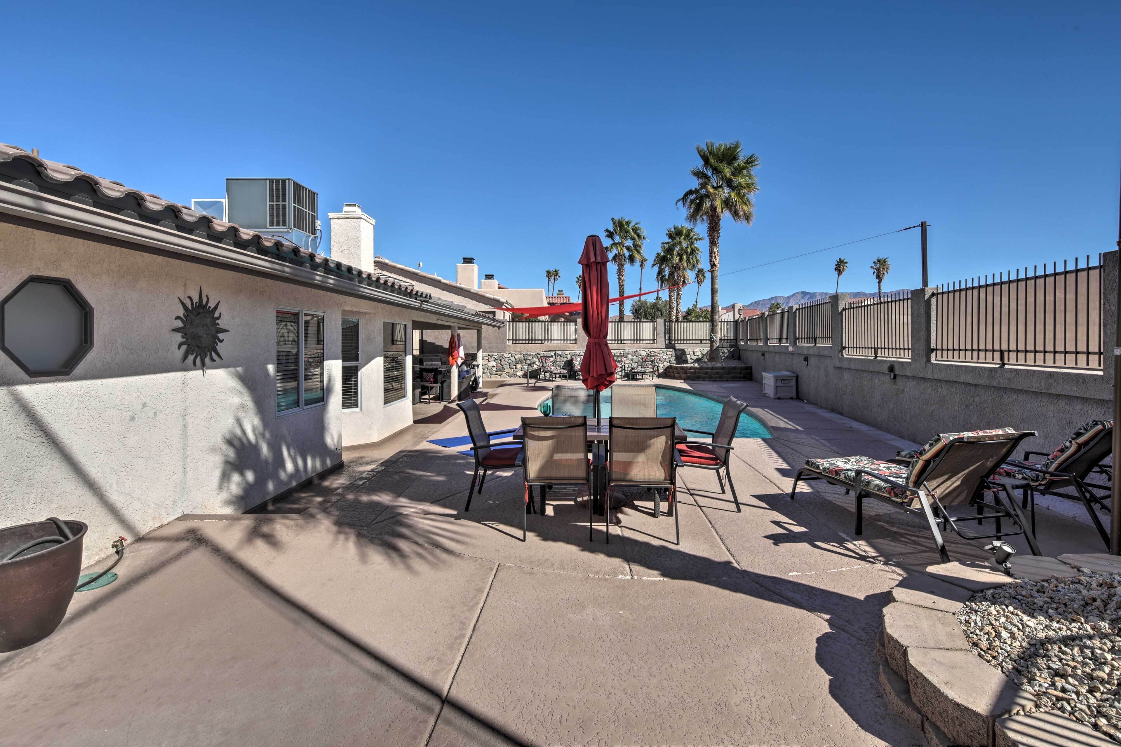An outdoor patio with a pool, lounge chairs, and a table.