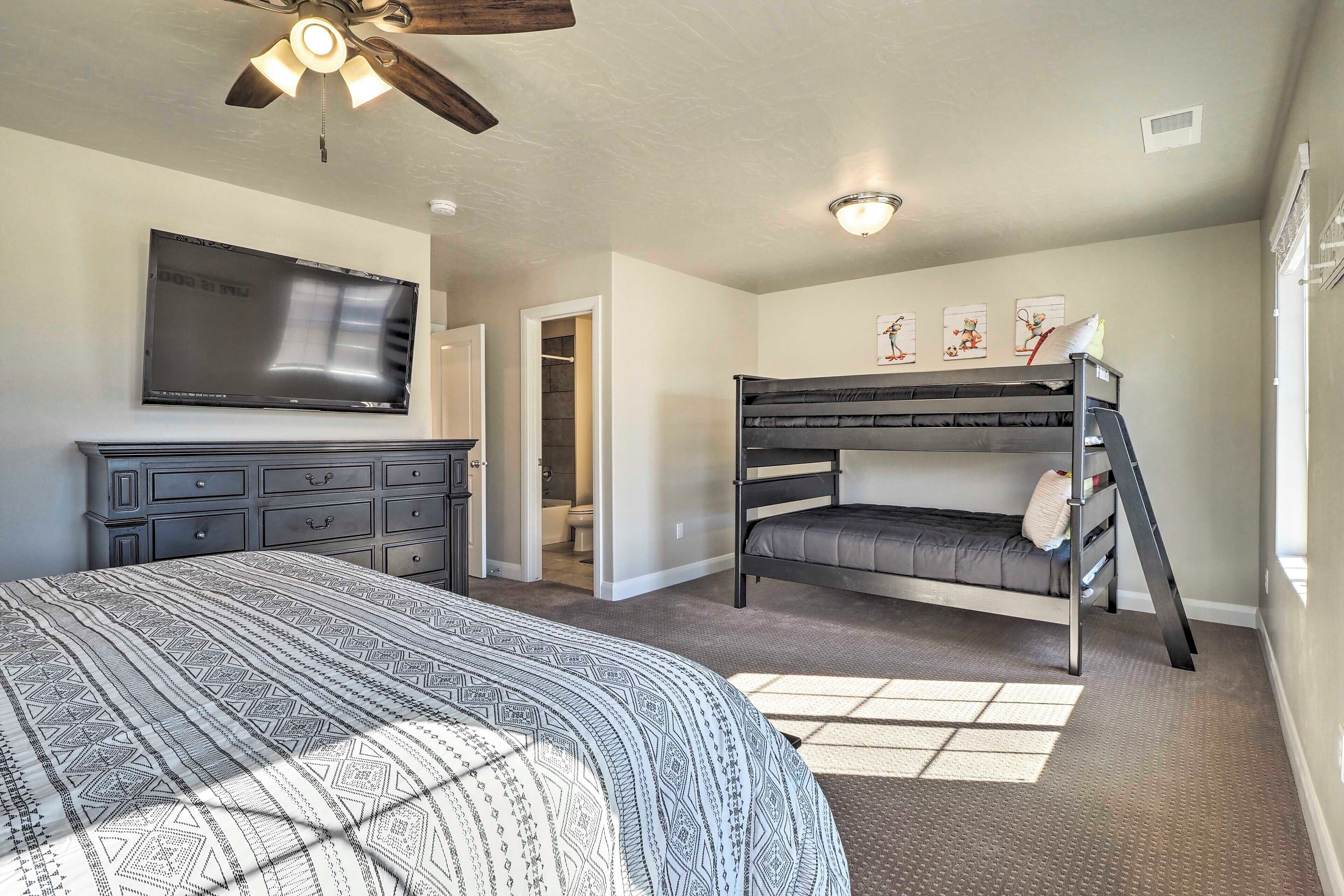 A bedroom with a bunk bed, a large bed, a dresser, a television, and a ceiling fan.