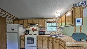 Una cocina con armarios de madera, un refrigerador, estufa, microondas y un lavamanos. Hay un cartel de bienvenida y una pizarra con la frase 'Escribe algo'.