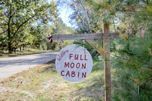 Uma placa de madeira com a inscrição 'Welcome Full Moon Cabin', pendurada em um poste com cerca de madeira.