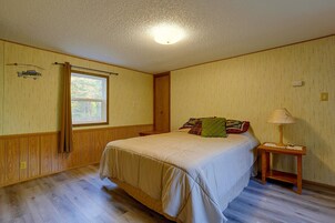 Quarto com cama, mesa de cabeceira, luminária, janela e termostato fixado na parede.