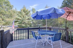 Um deck de madeira com mesa, cadeiras, um guarda-sol e uma bandeira.