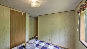 A bedroom with a checkered bedspread, wooden wardrobe, and a window with curtains.