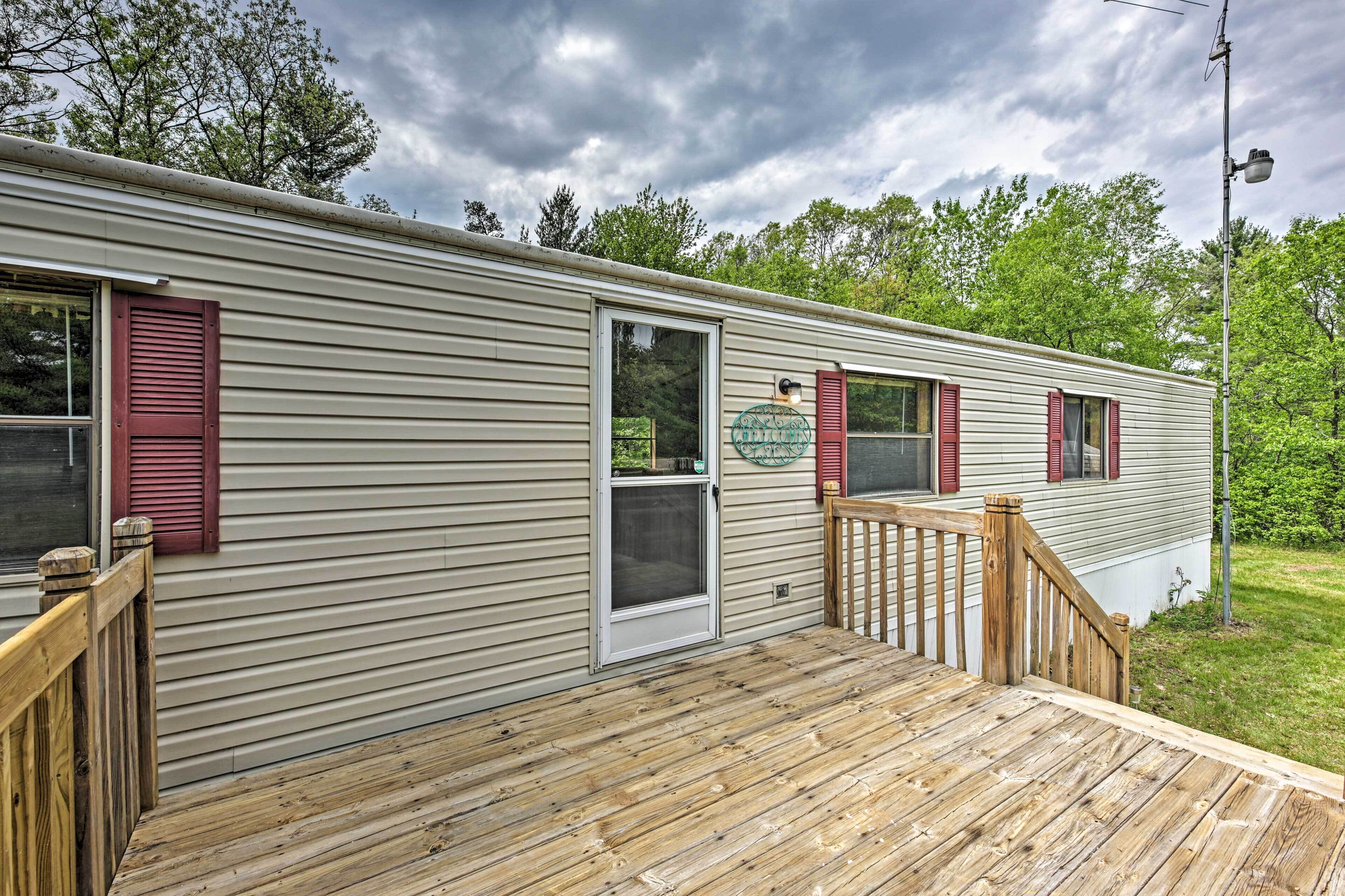 A mobile home with a wooden deck, a door, and a window with shutters.
