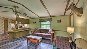 Interior de una cabaña con kitchenette, un sofá, una mesita de centro y una cabeza de venado montada en la pared.