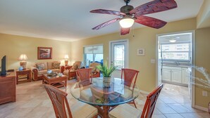 A spacious living room with a glass-top dining table surrounded by wicker chairs, a ceiling fan, and a large window providing natural light. - Oceanfront Bonita Beach Condo w/ Pool Access! (Bonita Springs)