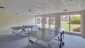 A room with two ping pong tables, a ceiling with recessed lighting, and a view of a garden through large windows. - Oceanfront Bonita Beach Condo w/ Pool Access! (Bonita Springs)