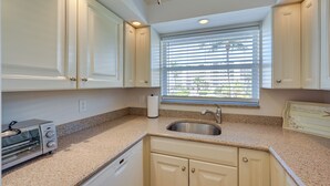 A kitchen with white cabinets, a stainless steel sink, a built-in toaster, and a window with blinds. - Oceanfront Bonita Beach Condo w/ Pool Access! (Bonita Springs)