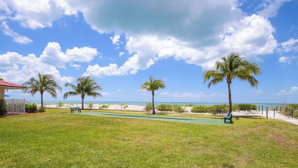 A grassy area with palm trees, a bench, and a view of the beach. - Oceanfront Bonita Beach Condo w/ Pool Access! (Bonita Springs)