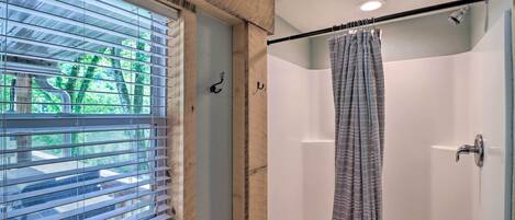 Un baño con ducha, una ventana con persianas y una cortina.
