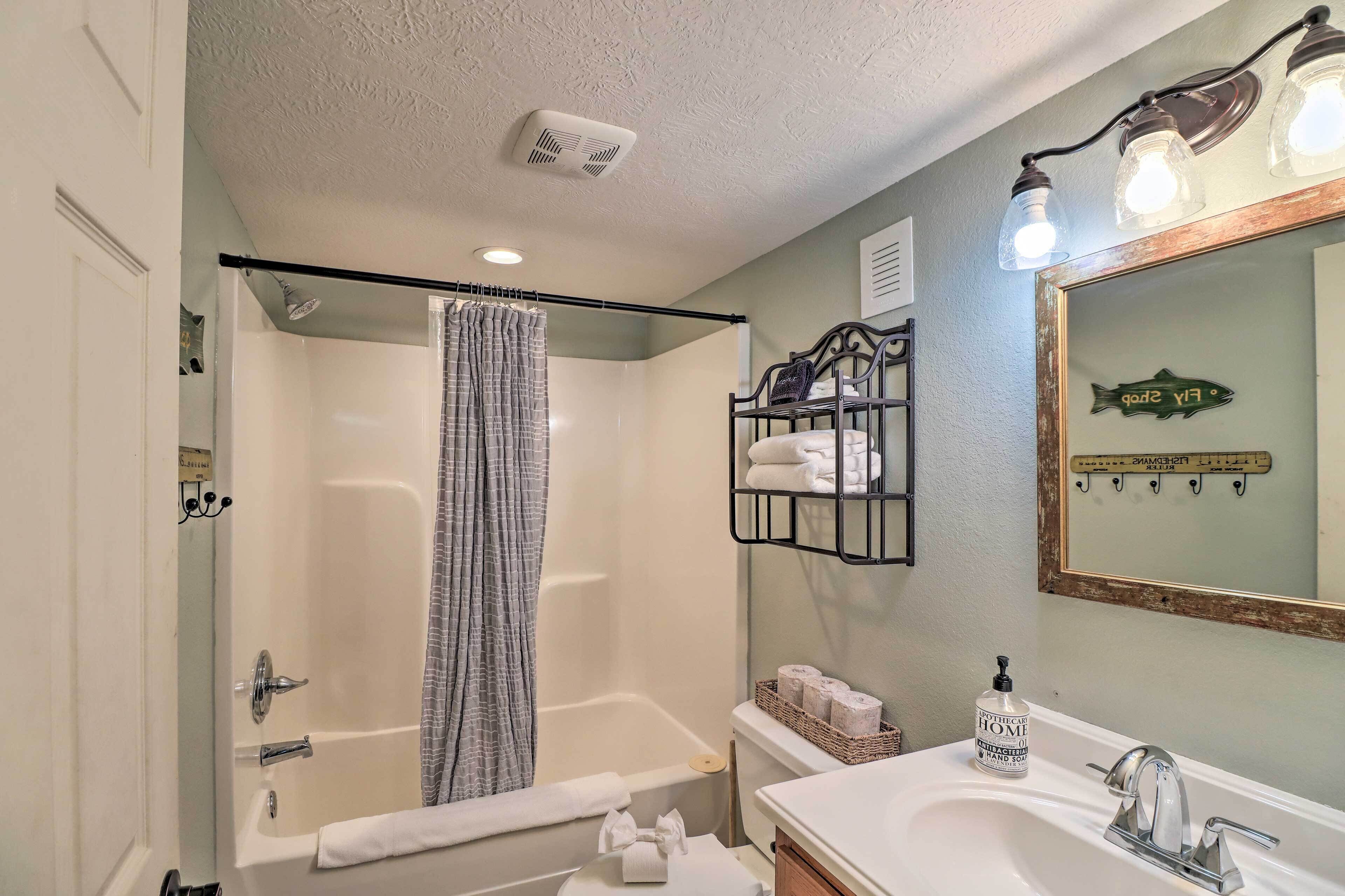 A bathroom with a bathtub, a shower curtain, a sink, and a mirror with a fish decoration.