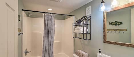 A bathroom with a bathtub, a shower curtain, a sink, and a mirror with a fish decoration.