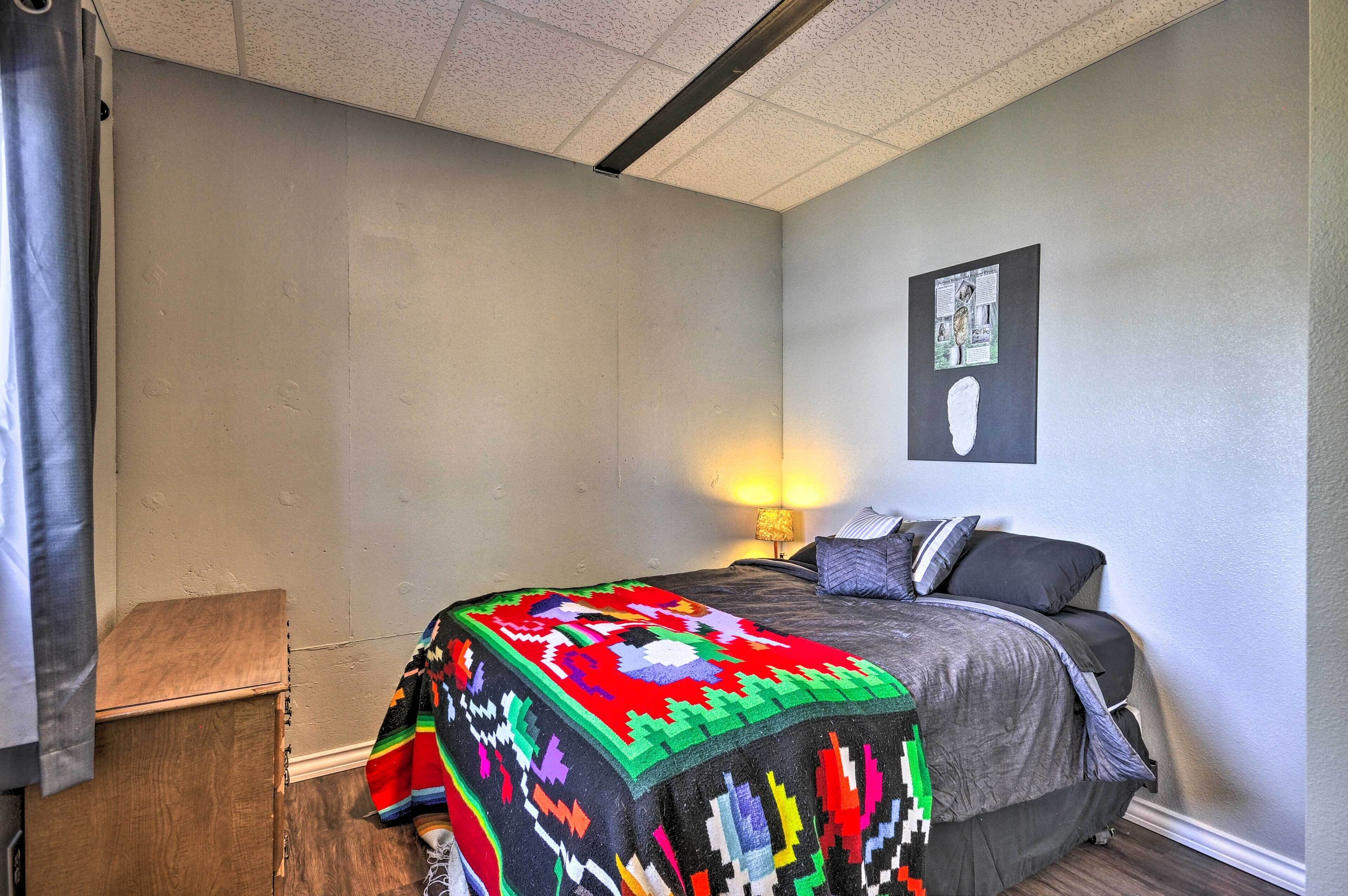 A bedroom with a bed, a bedside lamp, a wall-mounted picture, and a wooden nightstand.