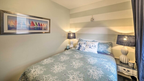 A bedroom with a bed, two bedside tables, a wall-mounted lamp, a framed picture, and a striped ceiling.