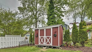 A red shed with white trim, a white picket fence, and a bicycle in a backyard with trees and a house in the background.