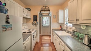 A compact kitchen with white cabinets, a white refrigerator, a stove, and a sink. There are two wooden mats on the floor, a window with blinds, and a door with a sign above it.