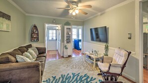 A living room with a brown sofa, a patterned rug, a ceiling fan, and a television.