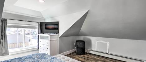 A bedroom with a bed, a television on a stand, a heater, and a window with curtains.