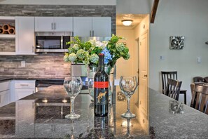 Un comptoir de cuisine avec une bouteille de vin, deux verres et un vase de fleurs.