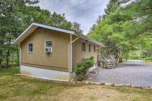 Une petite cabane à un seul étage, avec un toit en pente, un porche à l’avant et une allée gravillonnée.