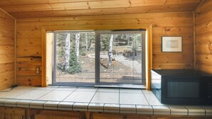 A wooden cabin interior with a large sliding glass door leading to a forested area, a microwave on the counter, and a framed certificate on the wall. - Near Natl Parks! Secluded Duck Creek Village Gem (Duck Creek Village)