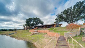 A lakeside property with a wooden deck, a covered patio, and a stone retaining wall.