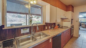 A kitchen with wooden cabinets, a double sink, and a window overlooking a scenic outdoor area.