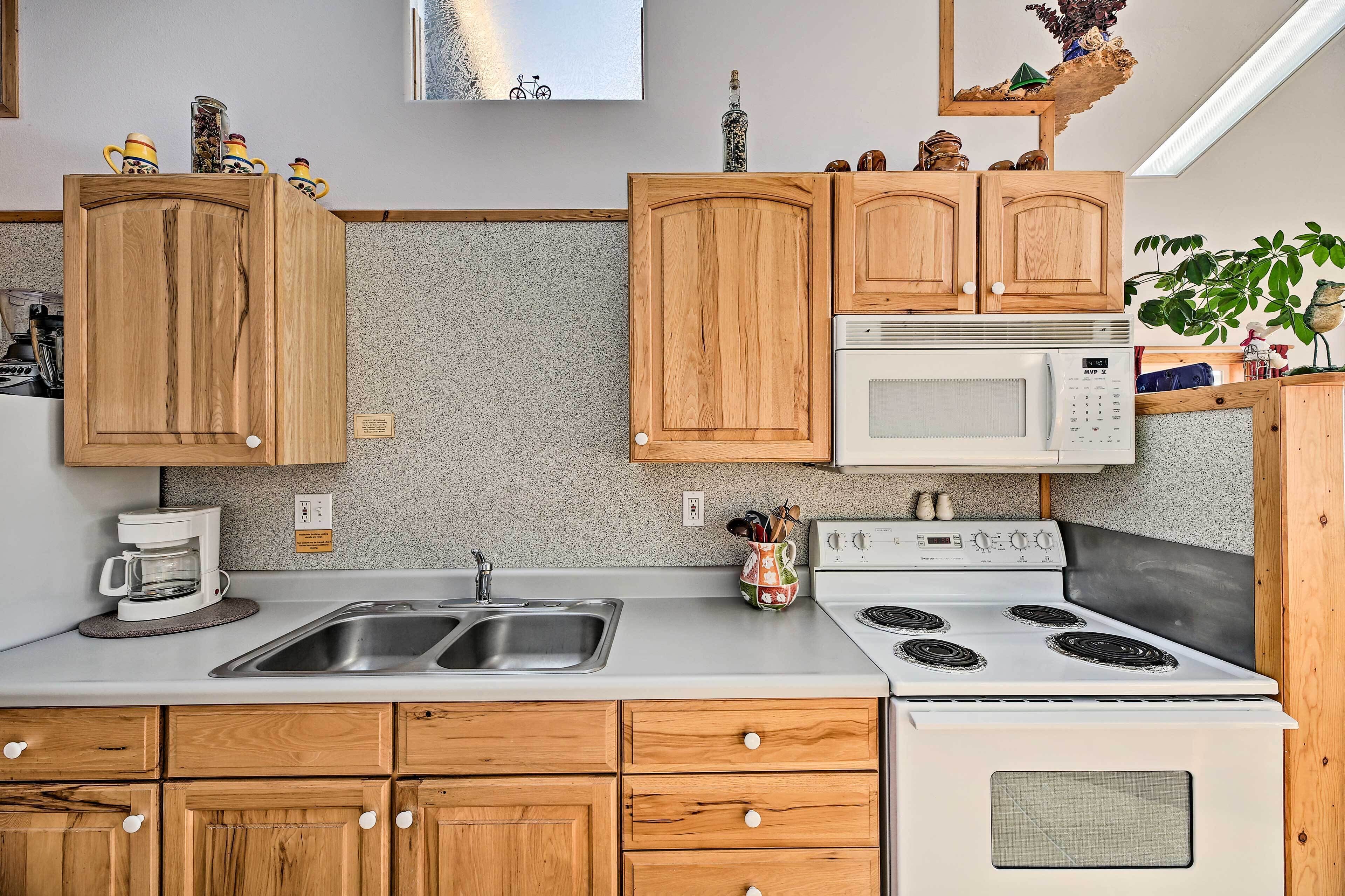 A kitchen with wooden cabinets, a microwave, a stove, a sink, and a coffee maker.