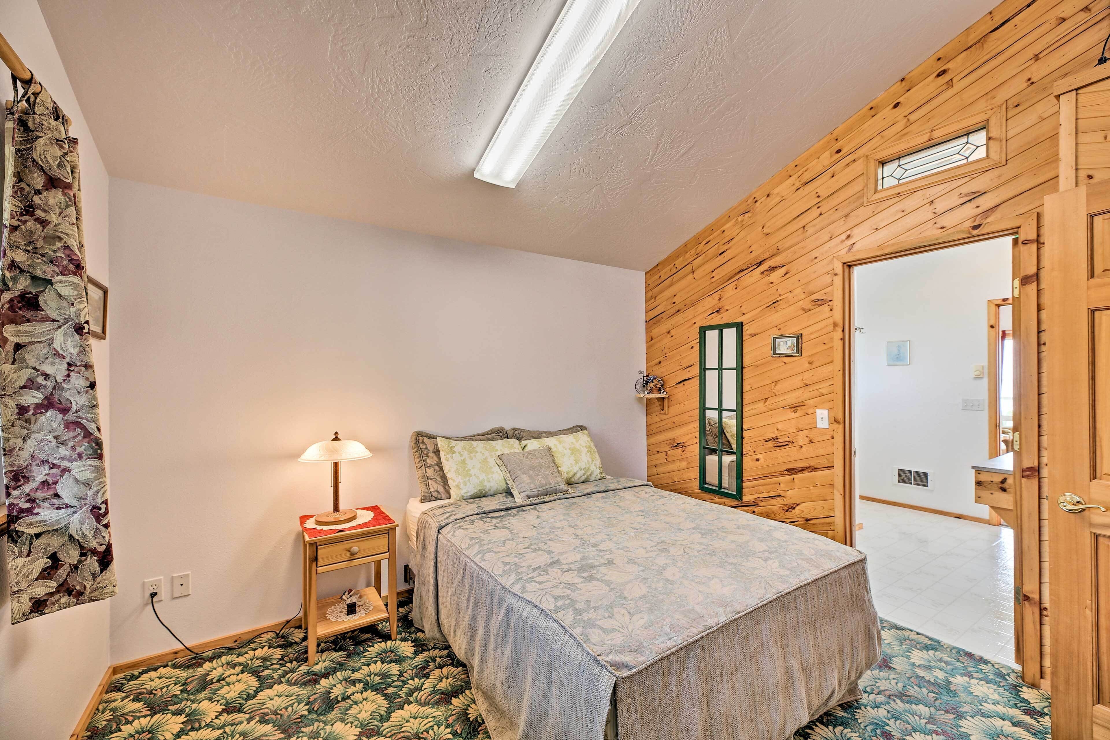 Ein Schlafzimmer mit einem Bett, einem Nachttisch, einer Lampe, einem blumigen Vorhang und Holzwänden.