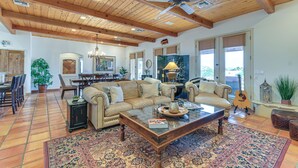 A spacious living room with a high ceiling, wooden beams, a large sofa, a coffee table, and a dining area with chairs and a table. - Private Pool, Spa, & Grills: Lake Havasu City Home (Lake Havasu City)