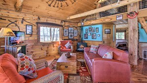 Ein rustikales Blockhaus-Interieur mit Holzwänden, Kamin, Sofa und Fernseher.