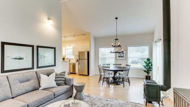 A modern living room with a grey sofa, a dining table with chairs, and a kitchen in the background. - Steps to Beach! Airy Coastal Escape w/ Deck (Pacific Beach)