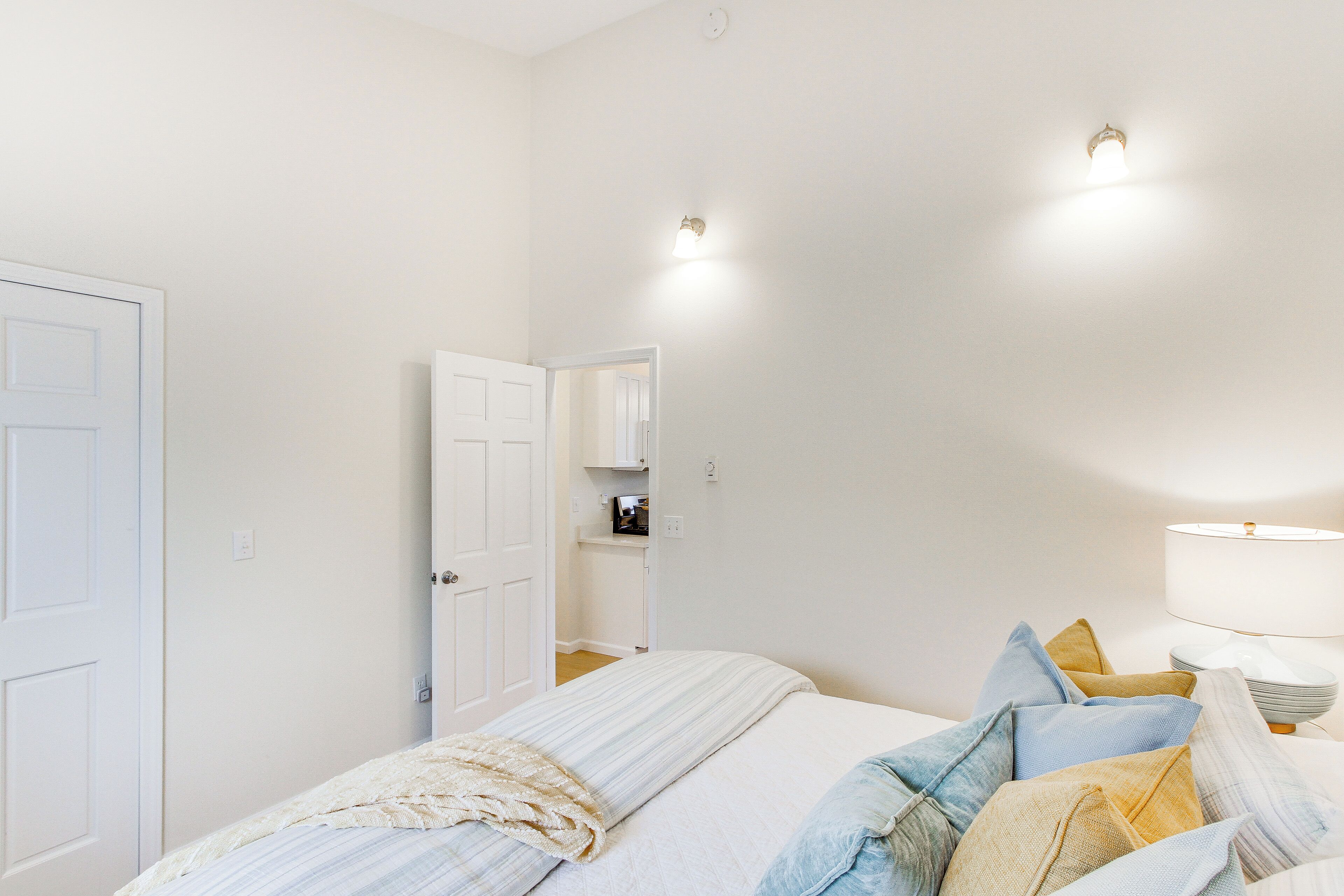 A bedroom with a bed, pillows, a bedside table, a lamp, and a door.