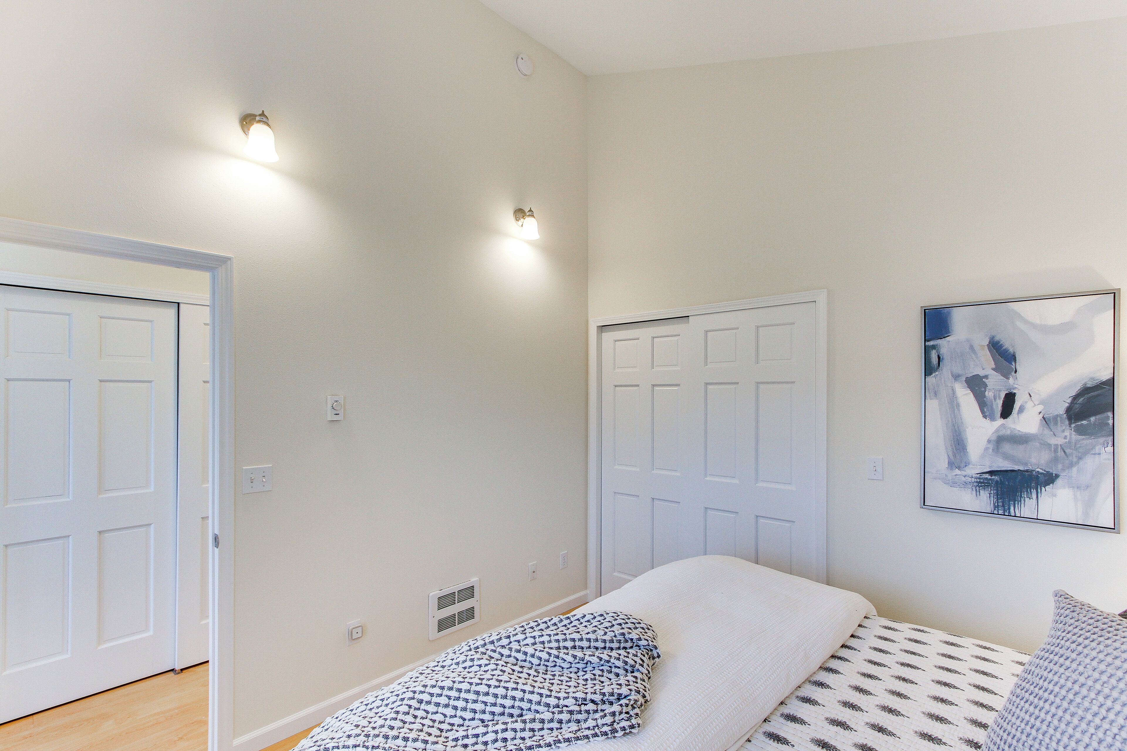 Une chambre avec deux portes, un lit recouvert d’une literie à motifs et un tableau abstrait accroché au mur.