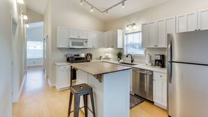A modern kitchen with white cabinets, stainless steel appliances, and a wooden island. - Steps to Beach! Airy Coastal Escape w/ Deck (Pacific Beach)