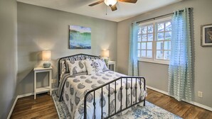 A bedroom with a bed, a ceiling fan, a window with curtains, and a painting on the wall. - Downtown Boerne Home on Cibolo Creek w/ Fire Pit (Boerne)